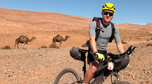 Bikepacking-Fahrer in Wüste mit Kamelen im Hintergrund
